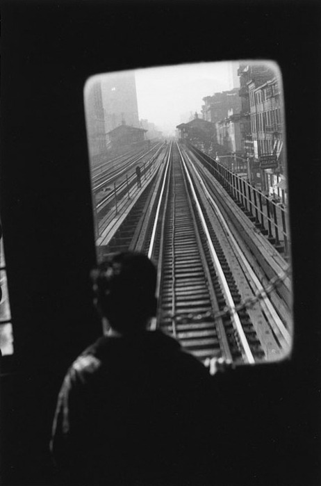 Fotografía en blanco y negro. Un niño mira por la ventana trasera del último vagón.