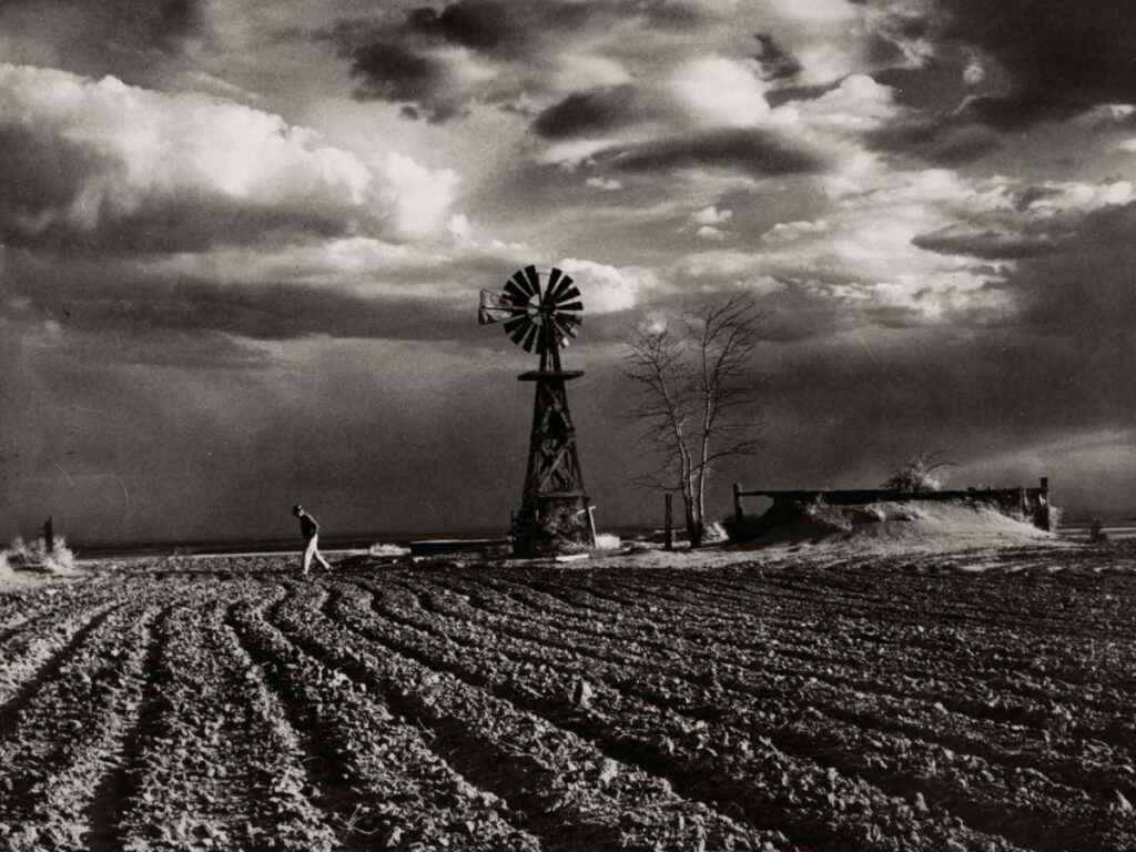 Fotografía en blanco y negro. Un hombre camina a través de un campo labrado en Colorado.